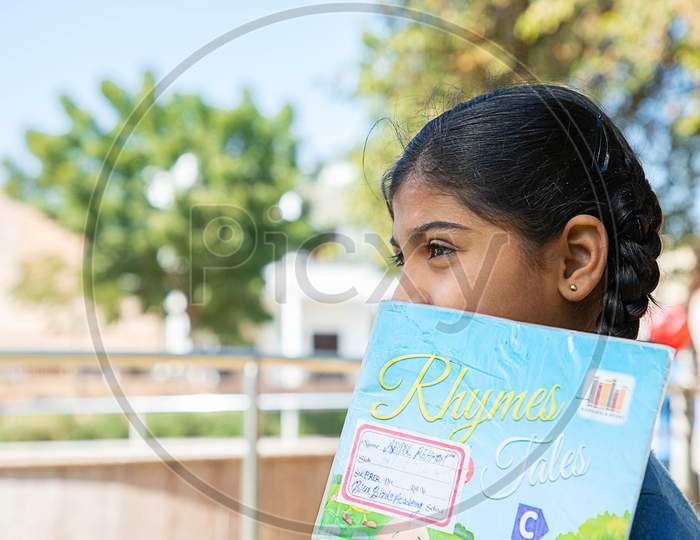 Jodhpur, Rajasthan, India - Jan 10Th 2020: Closeup Of Indian Happy Student School Girl Holding Exercise Notebook Cover Her Face, Standing Outdoor, Copy Space, Education Concept.