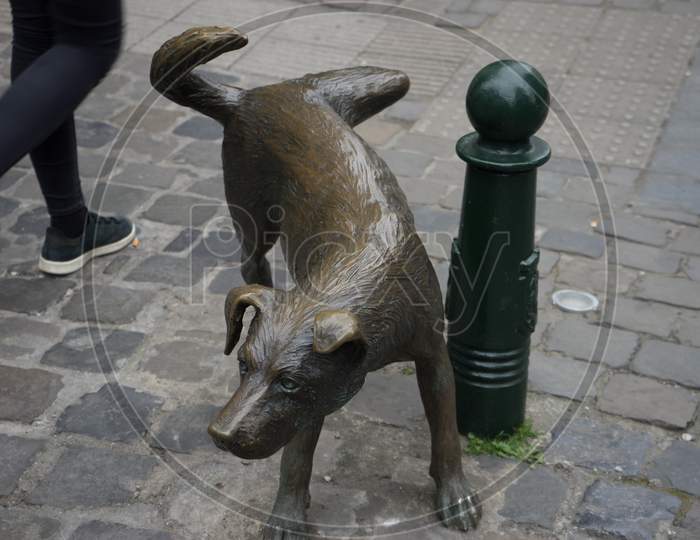 Image Of A Person Walks Past A Sculpture Of A Dog About To Pee On A 