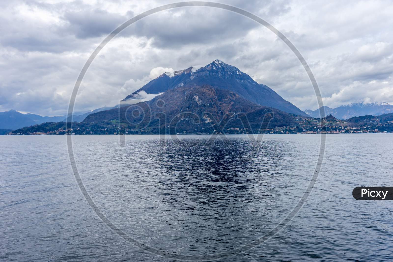 Italy, Varenna, Lake Como, A Large Body Of Water With A Mountain In The Background