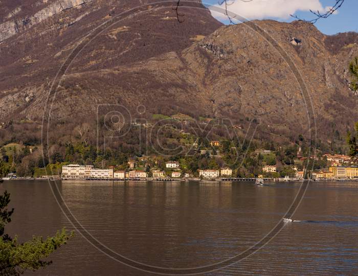 Italy, Bellagio, Lake Como, A Body Of Water With A Mountain In The Background