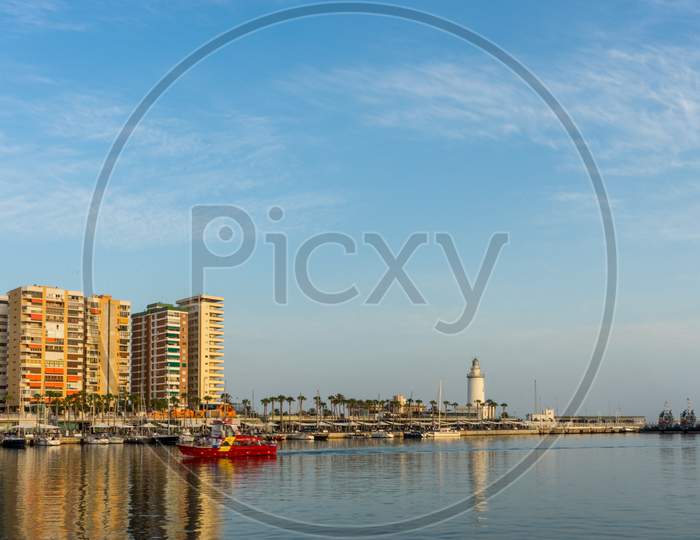 White Lighthouse And The Tall Buildings Of Malaga With Their Reflections In Malaga, Spain, Europe