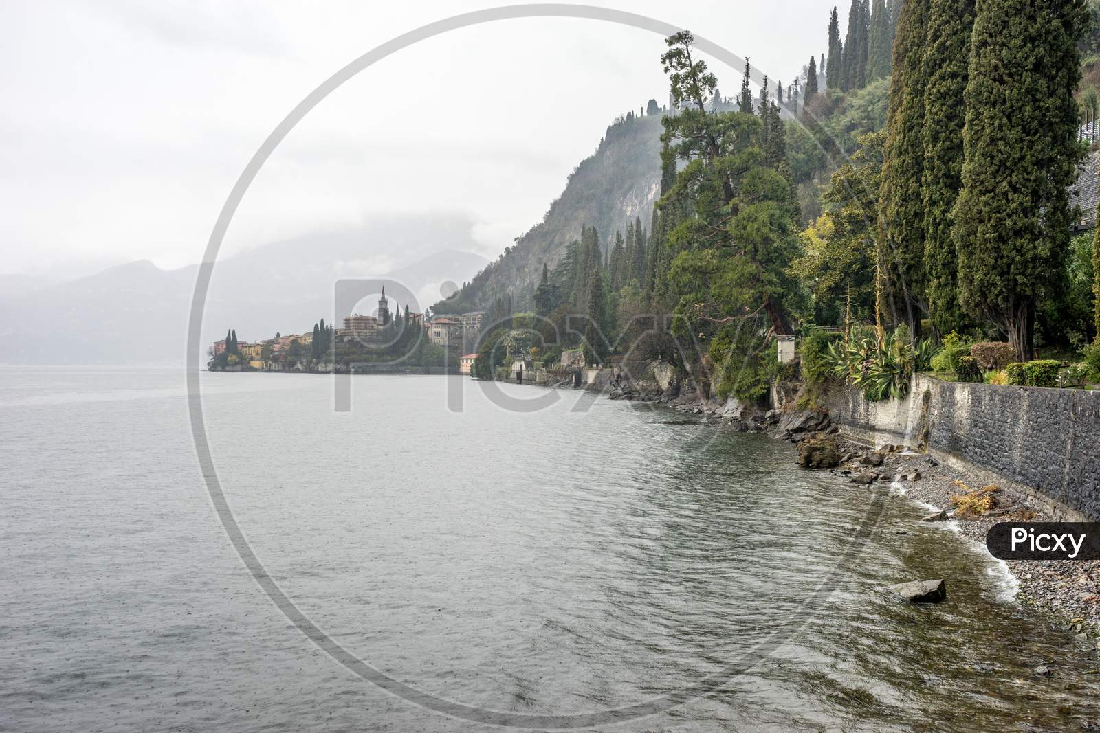 Italy, Varenna, Lake Como, A Large Body Of Water Surrounded By Trees