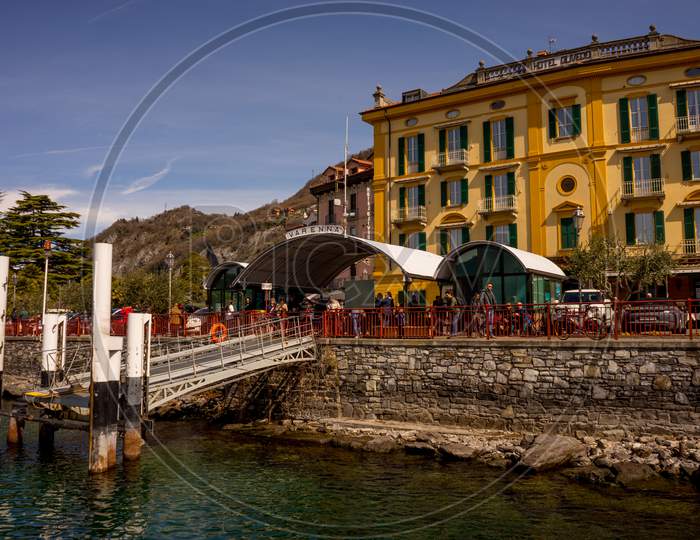 Menaggio, Italy-April 2, 2018: Varenna Waterside Dock At Quay With Hotel Ouvedo At Background
