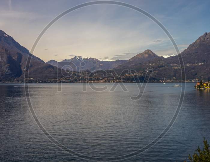 Italy, Menaggio, Lake Como, A Body Of Water With A Mountain In The Background