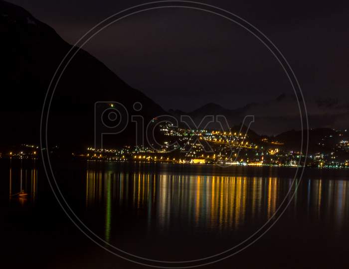 Italy, Varenna, Lake Como, A View Of A City At Night In Front Of A Body Of Water