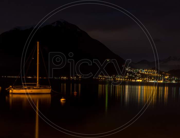 Italy, Varenna, Lake Como, A Large Body Of Water With A Boat In The Dark