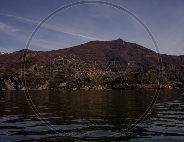 Italy, Menaggio, Lake Como, A Body Of Water With A Mountain In The Background