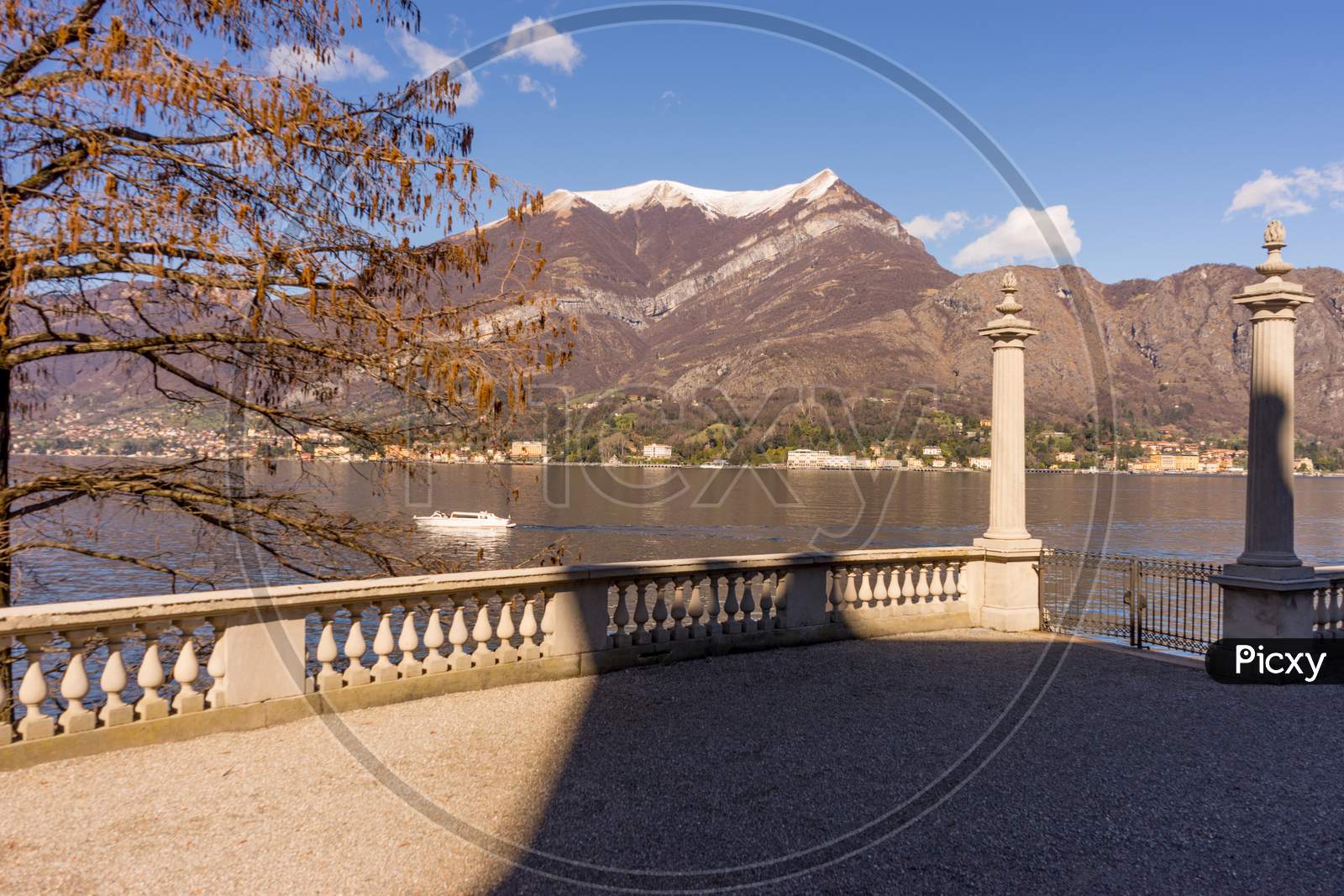 Italy, Bellagio, Lake Como, Fence Overlooking Scenic View Of Snowcapped Mountains Against Blue Sky, Lombardy