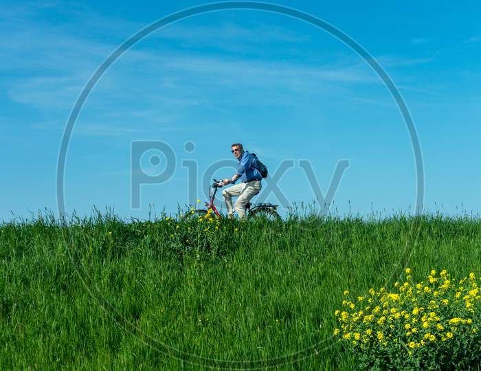 Netherlands,Amsterdam - 21 April 2017:  Man Cycliing On The Polder Wetlands Against A Blue Sky