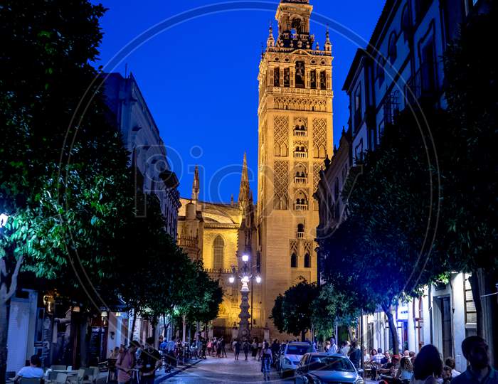 Seville, Spain- June 18, 2017:Tourists Walk On The Street At Night Next To The Giralda Bell Tower In Seville, Spain June 2017, Europe
