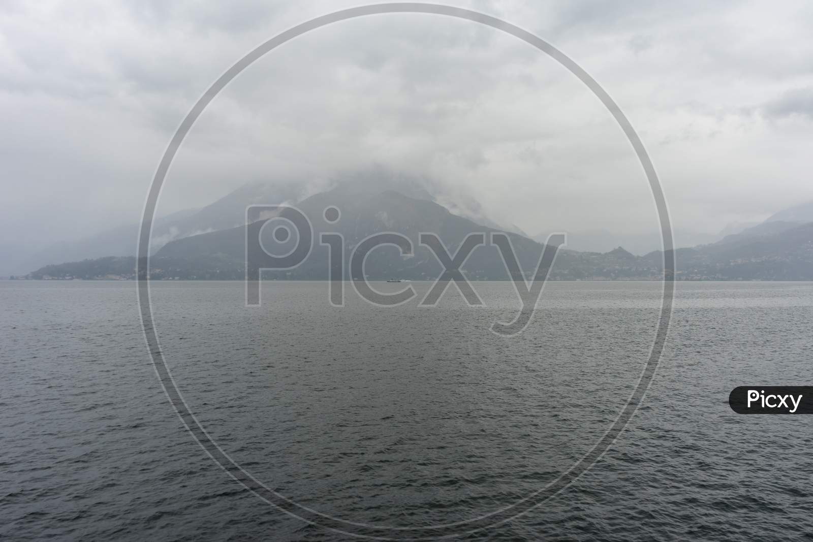 Italy, Varenna, Lake Como, A Body Of Water With A Mountain In The Background