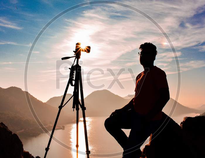 Silhouette of boy and camera with tripod and sunstar.