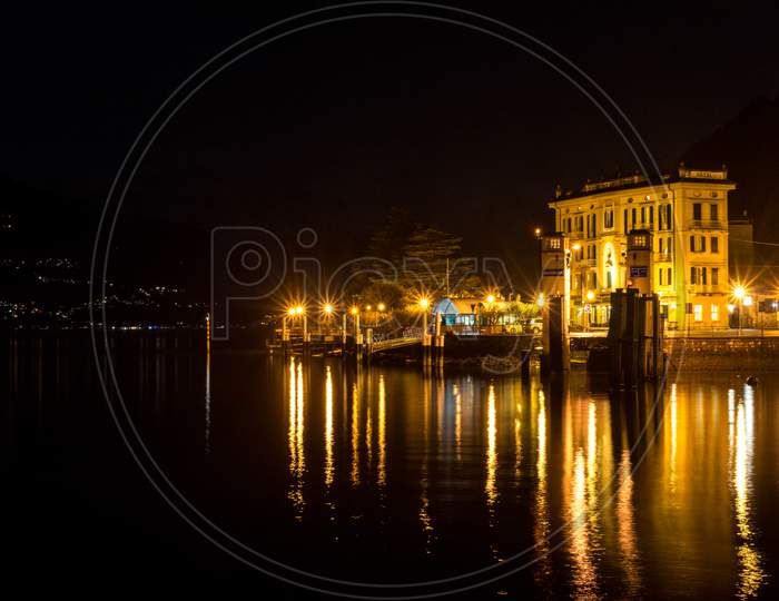 Italy, Varenna, Lake Como, A Body Of Water With A City In The Night Sky
