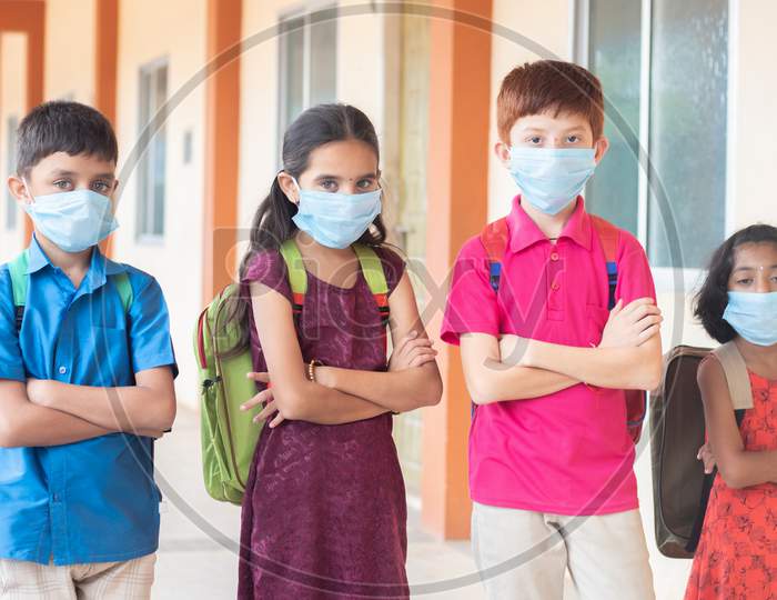 Children In Medical Mask With School Backpack Standing With Arms Crossed By Looking To The Camera- Concept Of Back To School And Reopen.