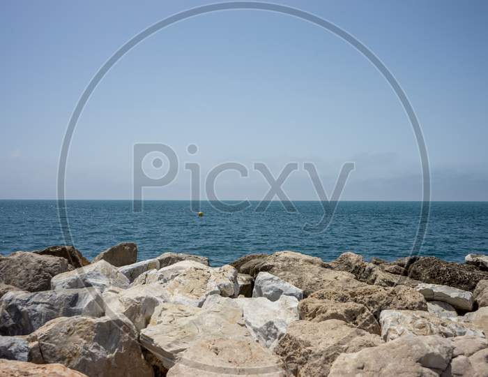 Rocks Against The Green Ocean At Malagueta Beach In Malaga, Spain, Europe With Clear Sky