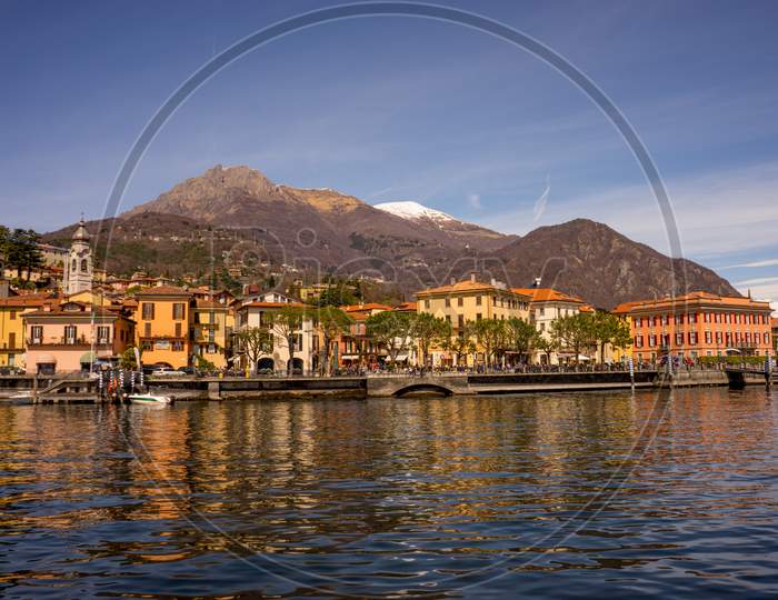 Italy, Menaggio, Lake Como, A Boat Is Docked Next To A Body Of Water