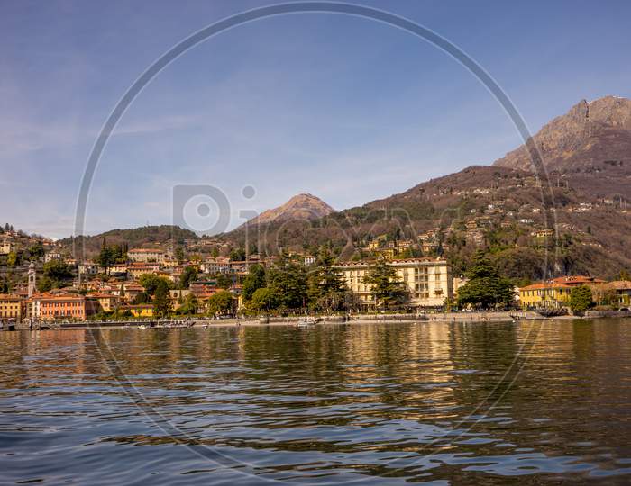 Italy, Menaggio, Lake Como, A Large Body Of Water With A Mountain In The Background