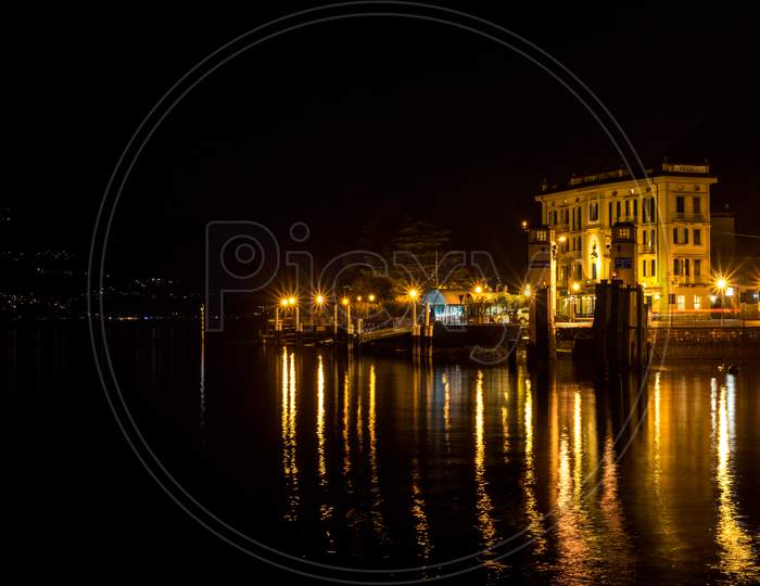 Italy, Varenna, Lake Como, A Body Of Water With A City In The Night Sky