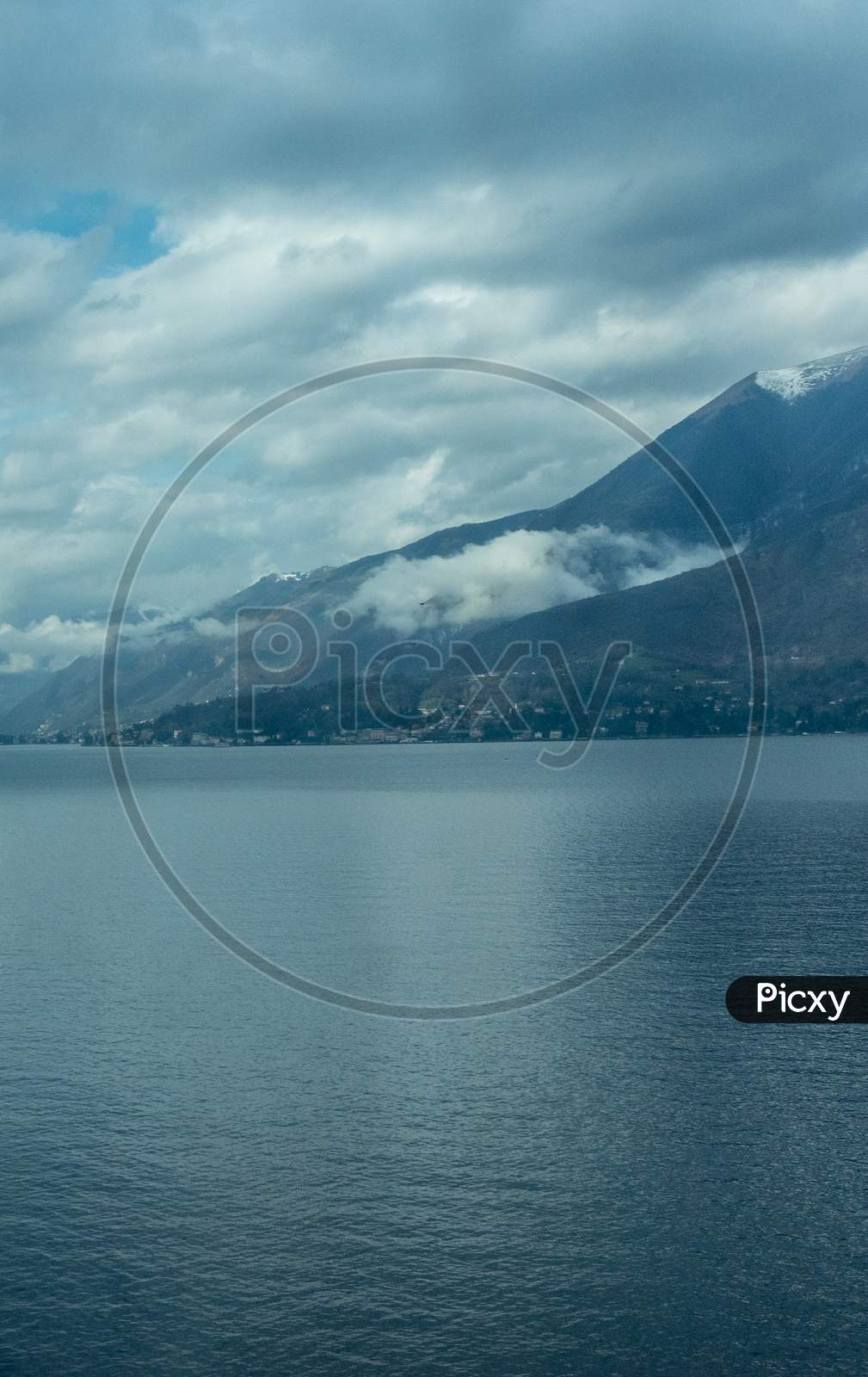 Italy, Varenna, Lake Como, A Large Body Of Water With A Mountain In The Background
