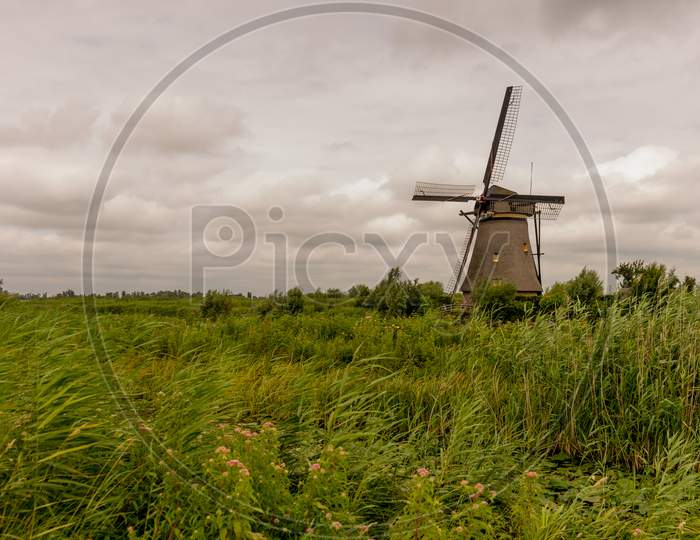 Netherlands, Rotterdam, Kinderdijk, Heritage Windmill Above Lush Green Grass Along A Canal