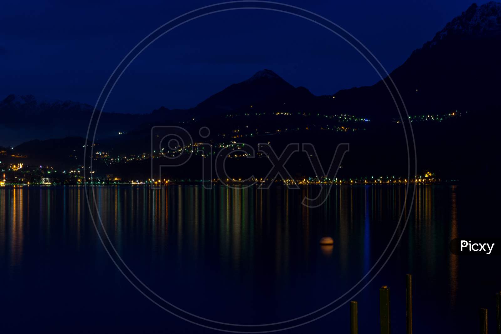 Italy, Varenna, Lake Como, A Large Body Of Water With A Mountain In The Dark