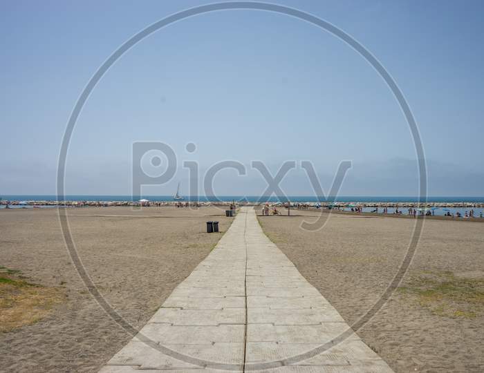 A Stone Pathway Leading To The Sea And Ocean At Malagueta Beach In Malaga, Spain, Europe On A Cloudy Moring With A Boat