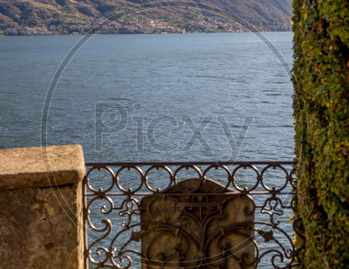 Italy, Lecco, Lake Como, A Stone Bench Sitting Next To A Body Of Water