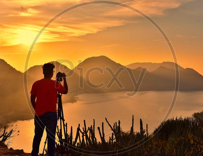 Silhouette of boy with camera and tripod during sunrise at Bahubali Hills udaipur.