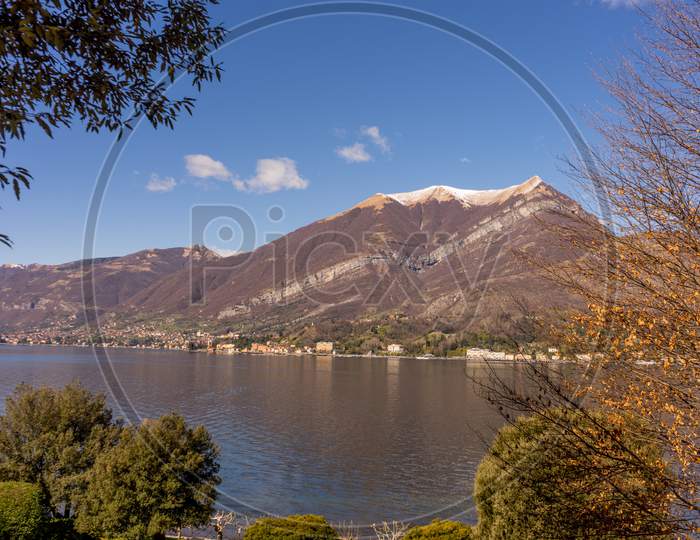 Italy, Bellagio, Lake Como, A Body Of Water With A Mountain In The Background