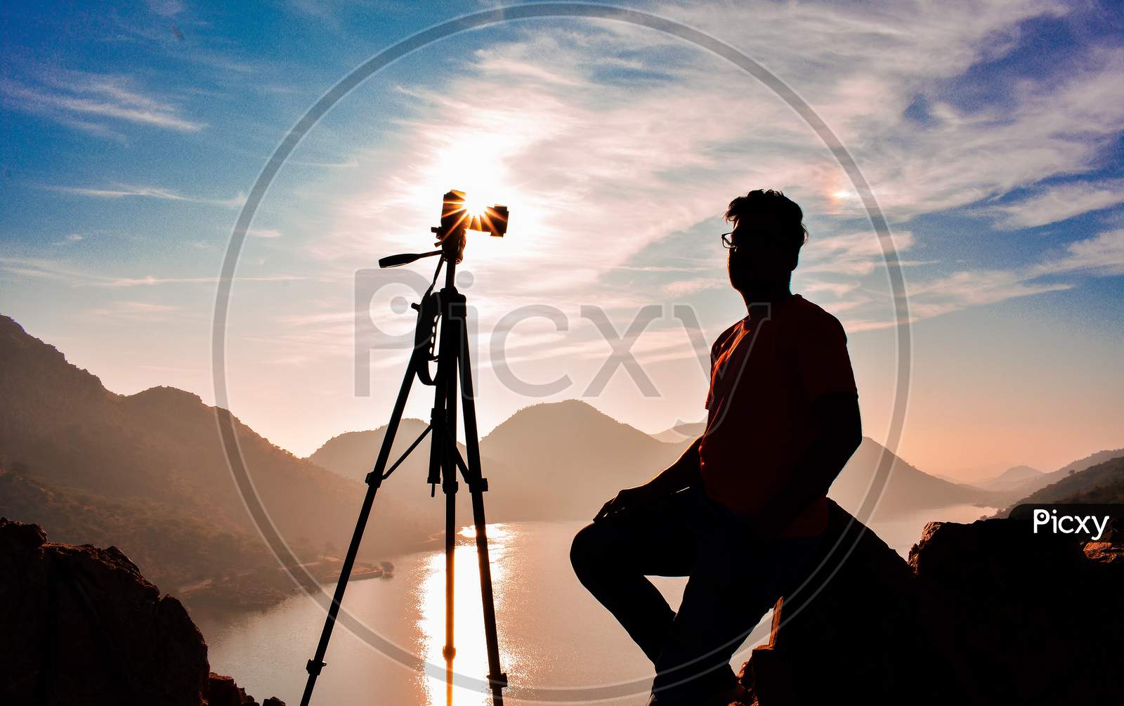 Silhouette of boy and camera with tripod and sunstar.