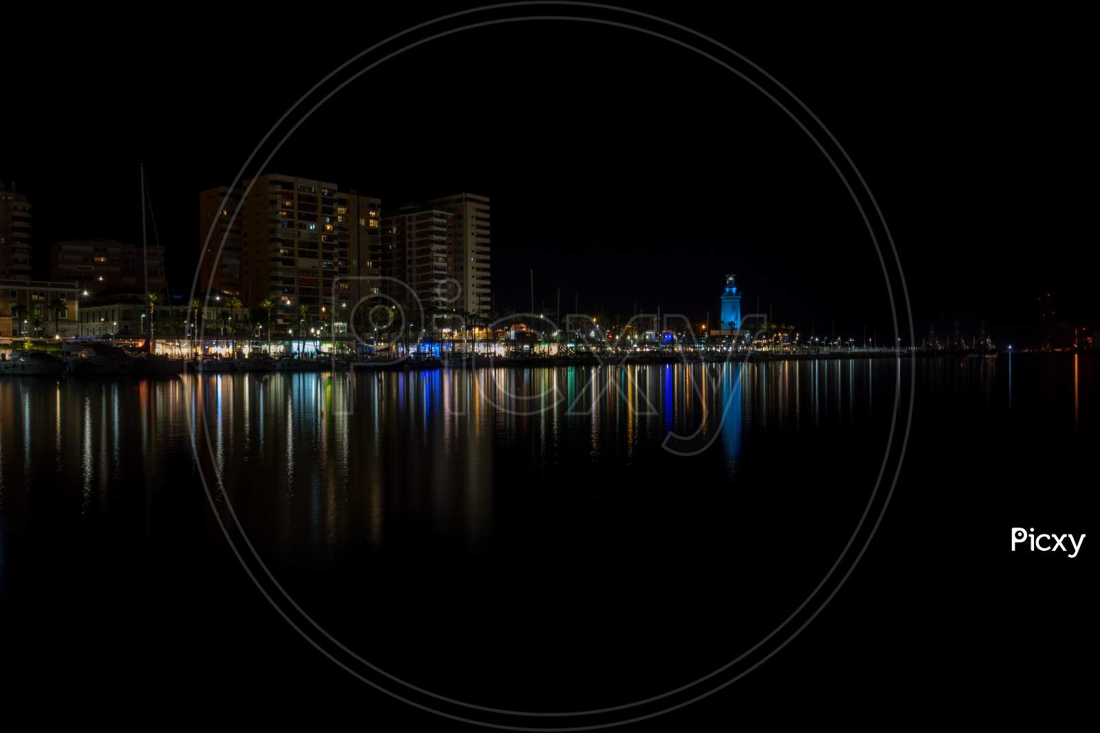 View Of Malaga City And Lighthouse And Their Reflections On Water From Harbour, Malaga, Spain, Europe At Night