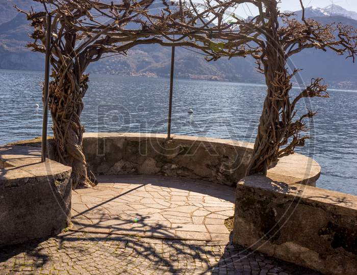 Italy, Menaggio, Lake Como, A Stone Bridge Over A Body Of Water