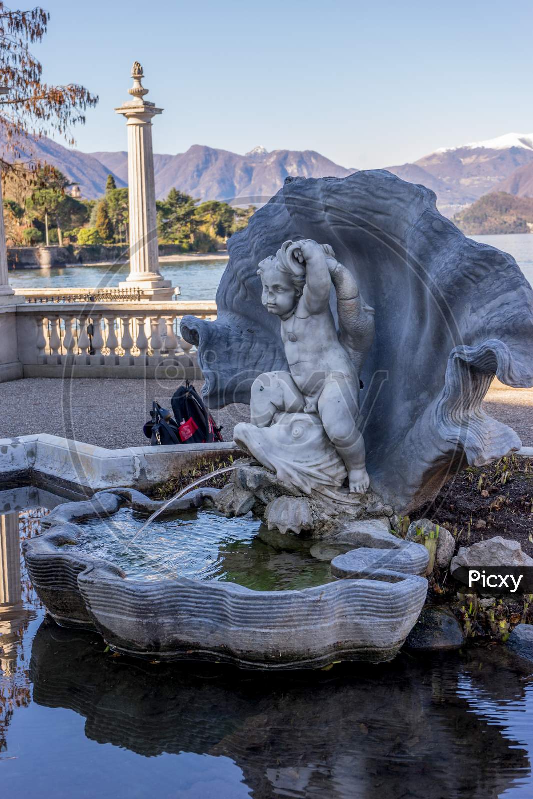 Italy, Bellagio, Lake Como, Abellagio, Italy-April 1, 2018: Water And Lily Fountain At Giardini Di Villa Melzi Group Of Stuffed Animals Sitting Next To A Body Of Water