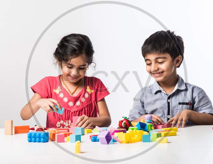 Indian Cute Kids Playing With Colourful Plastic Toys Or Blocks Against White Background