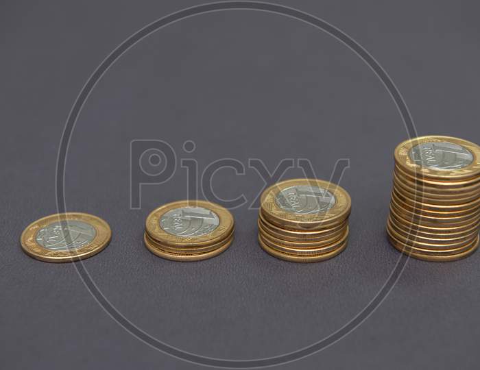 Stacks Of Golden And Silver Coins (1 Real) As In A Growing Graph, Representing Rise Or Fall On Black Bacground. Economy Concept. Copy Space. Selective Focus. Brazilian Coins