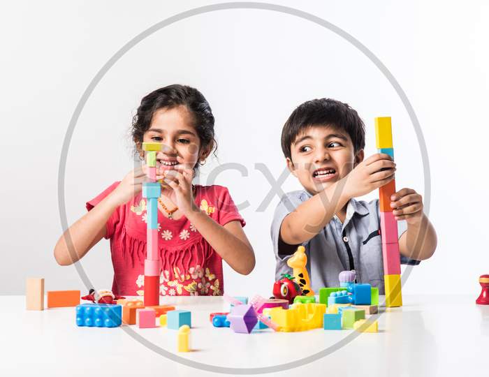 Indian Cute Kids Playing With Colourful Plastic Toys Or Blocks Against White Background