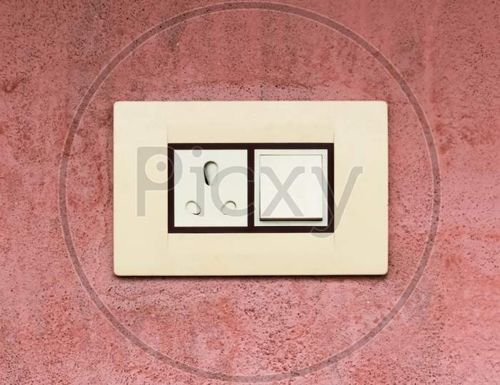 Modern electrical switch and three pin plug on maroon rough wall