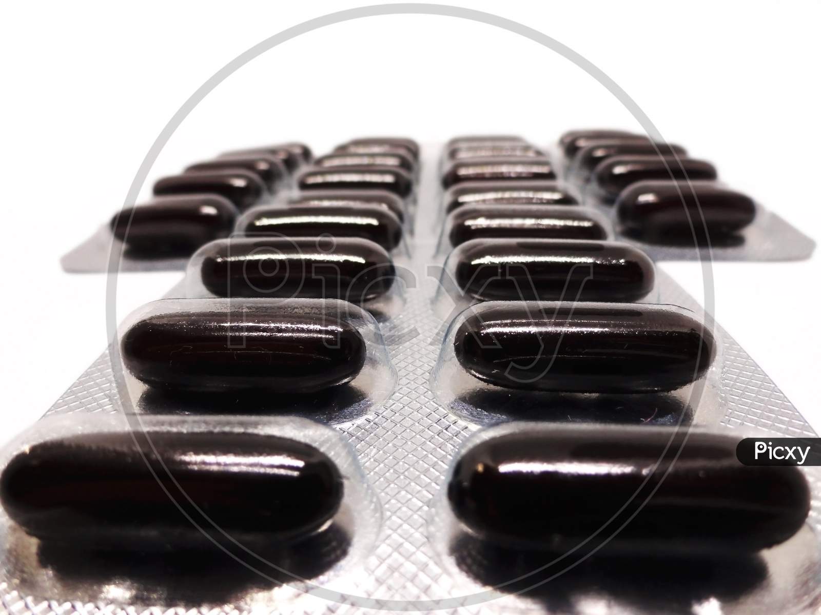 Black multi-vitamin capsules arranges in column on white background