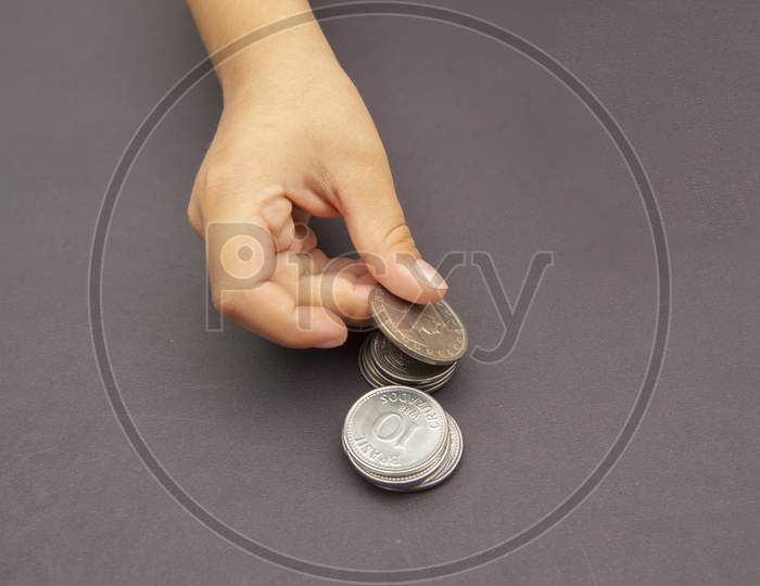 Kid Hands Putting Golden And Silver Coin On Pile Of Coins. Concept Of Saving And Spending Money. Future Investment. Long-Term Economic Planning. Selective Focus. Copy Space.