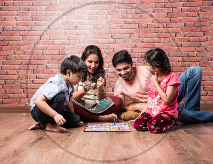 Indian Happy Family Playing Board Games Like Chess, Ludo Or Snack And Ladder At Home In Quarantine