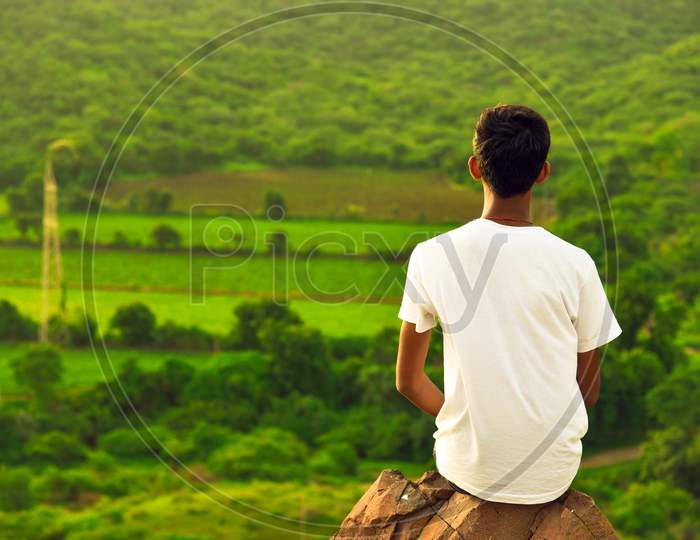Young Boy Sitting On Mountain Rock Back View .