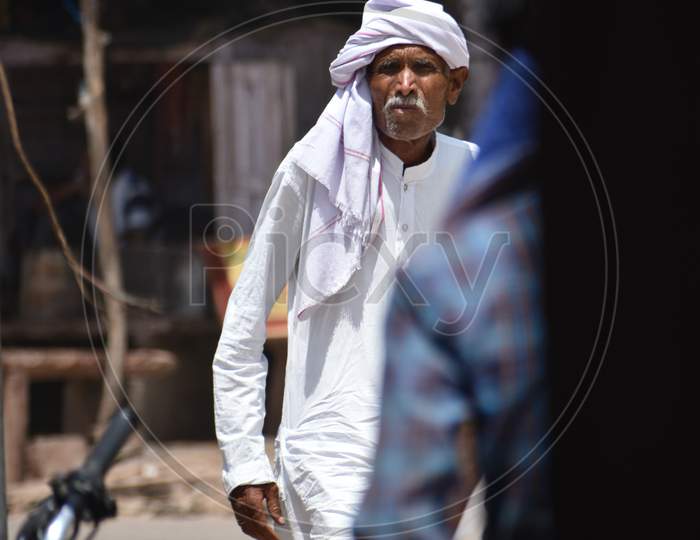 An indian old man walking on street of a town market.