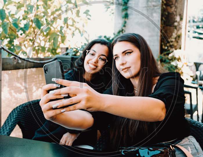 Couple Of Women Taking A Selfie With The Focus Put On The Phone While They Are Both Smiling And Out Of Focus