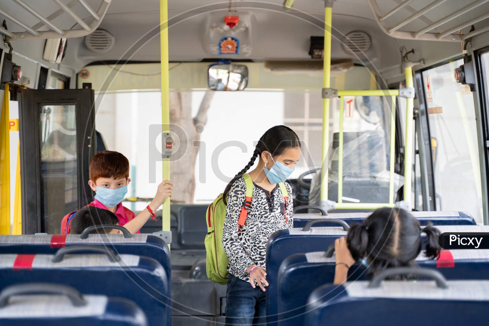 Kids With Medical Mask Coming Inside School Bus And Sitting On Seats While Maintaining Social Distance Due To Coronavirus Or Covid-19 Pandemic - Concept Of School Reopen Or Back To School