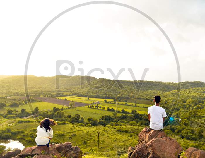 Young Girl And Boy Sitting On Mountain And Watching Sunset .