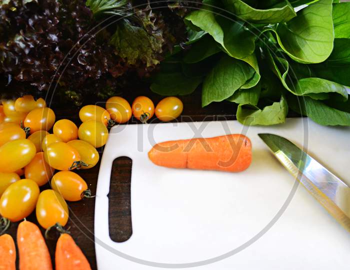 Organic Vegetables Ingredients Around White Cutting Board With Carrot And Knife