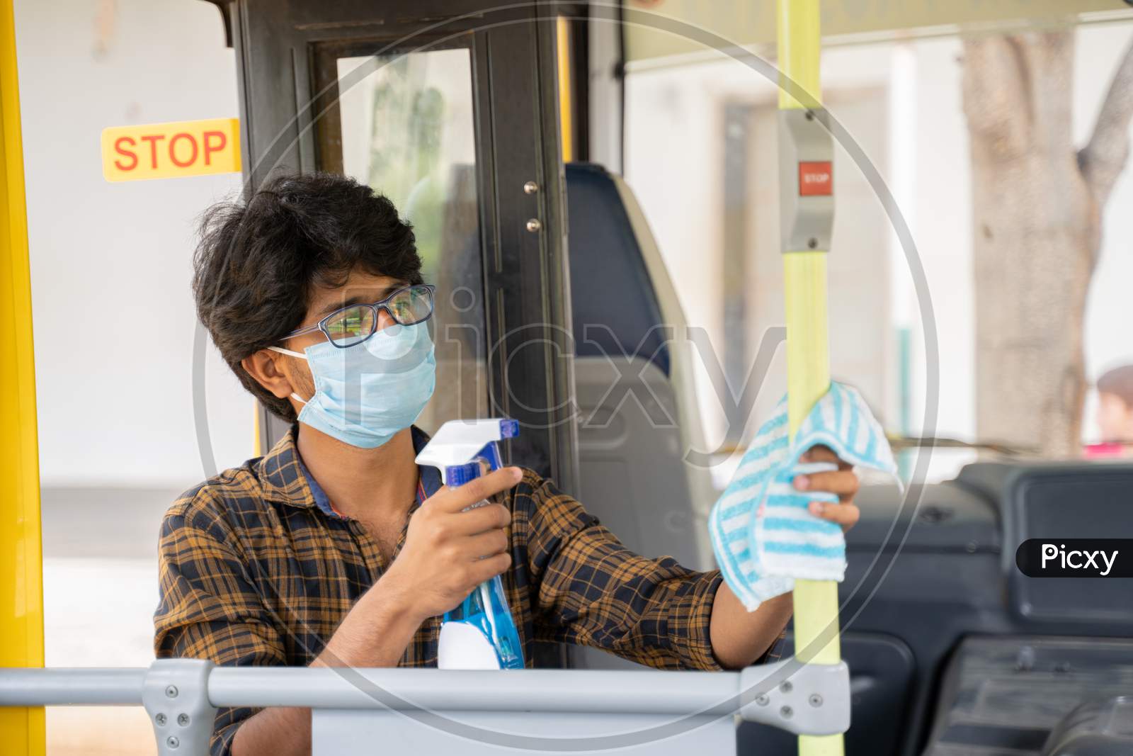 Young Man In Medical Mask Disinfecting Or Sanitizing Bus By Using Alcohol Disinfectant Spray To Protect People From Coronavirus Or Covid-19 Infection.