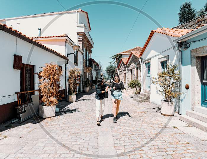 Two Women Walking Through The Streets Of A Ancient Portuguese Villa While Talking To Each Other