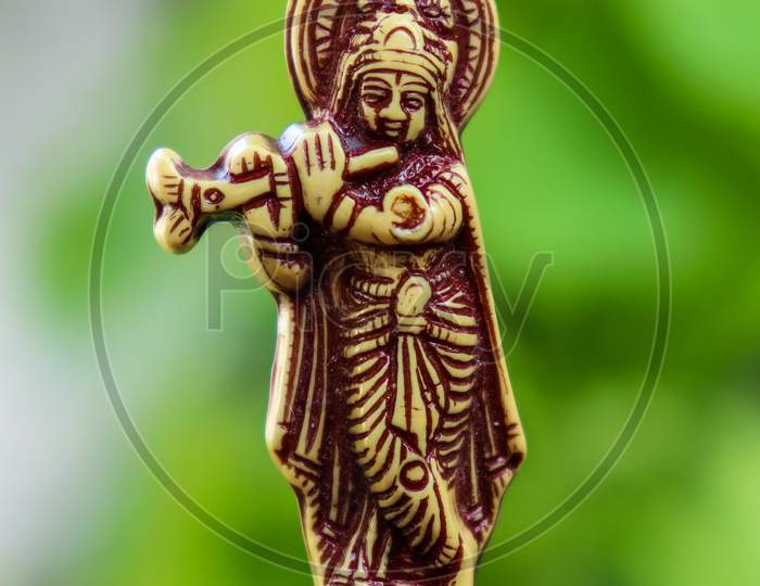 Yellow color lord krishna with flute idol in green beautiful background.