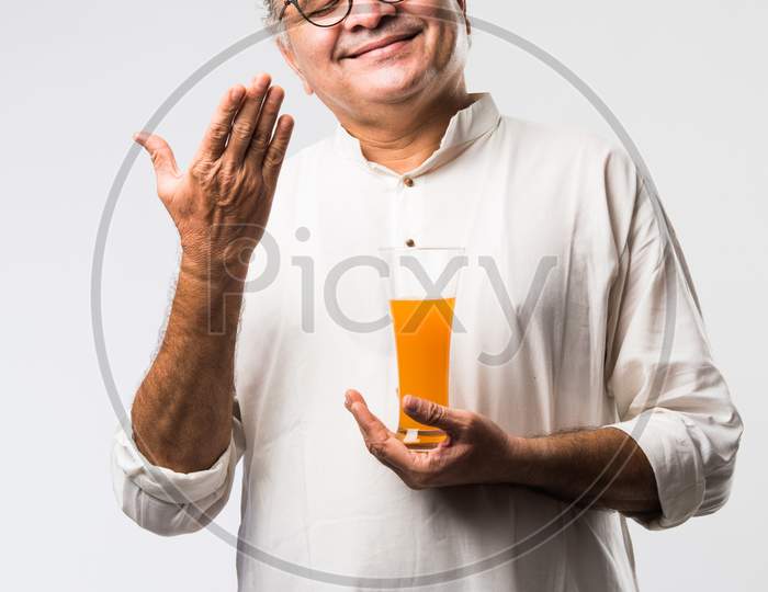 Indian Old Man  Holding Or Drinking Fresh Orange Or Mango Juice In Glass